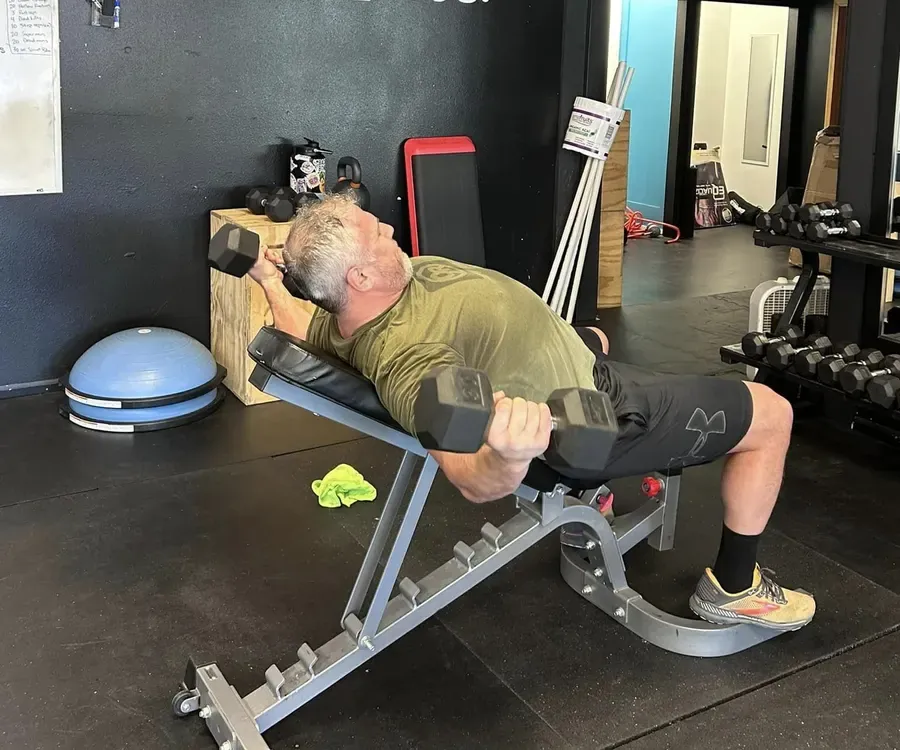 A member pressing dumbbells on an incline bench