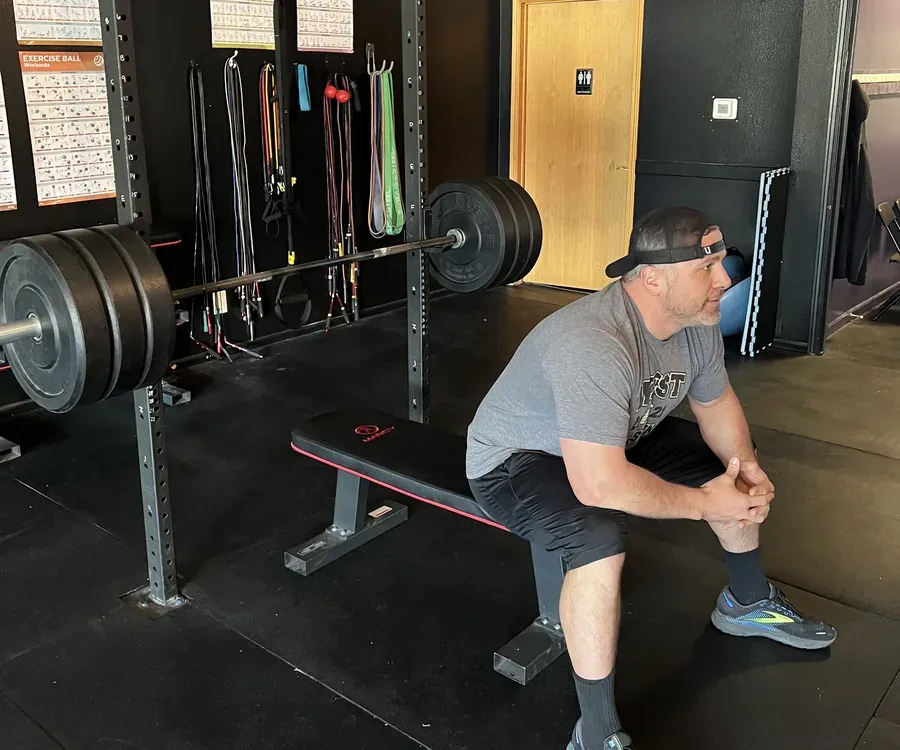 An athlete resting on a bench beside a loaded barbell between sets